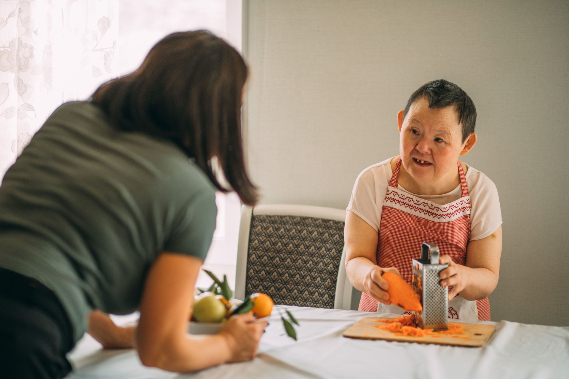Lifestyle, education. An elderly woman with down syndrome is studying in the kitchen or classroom with a teacher