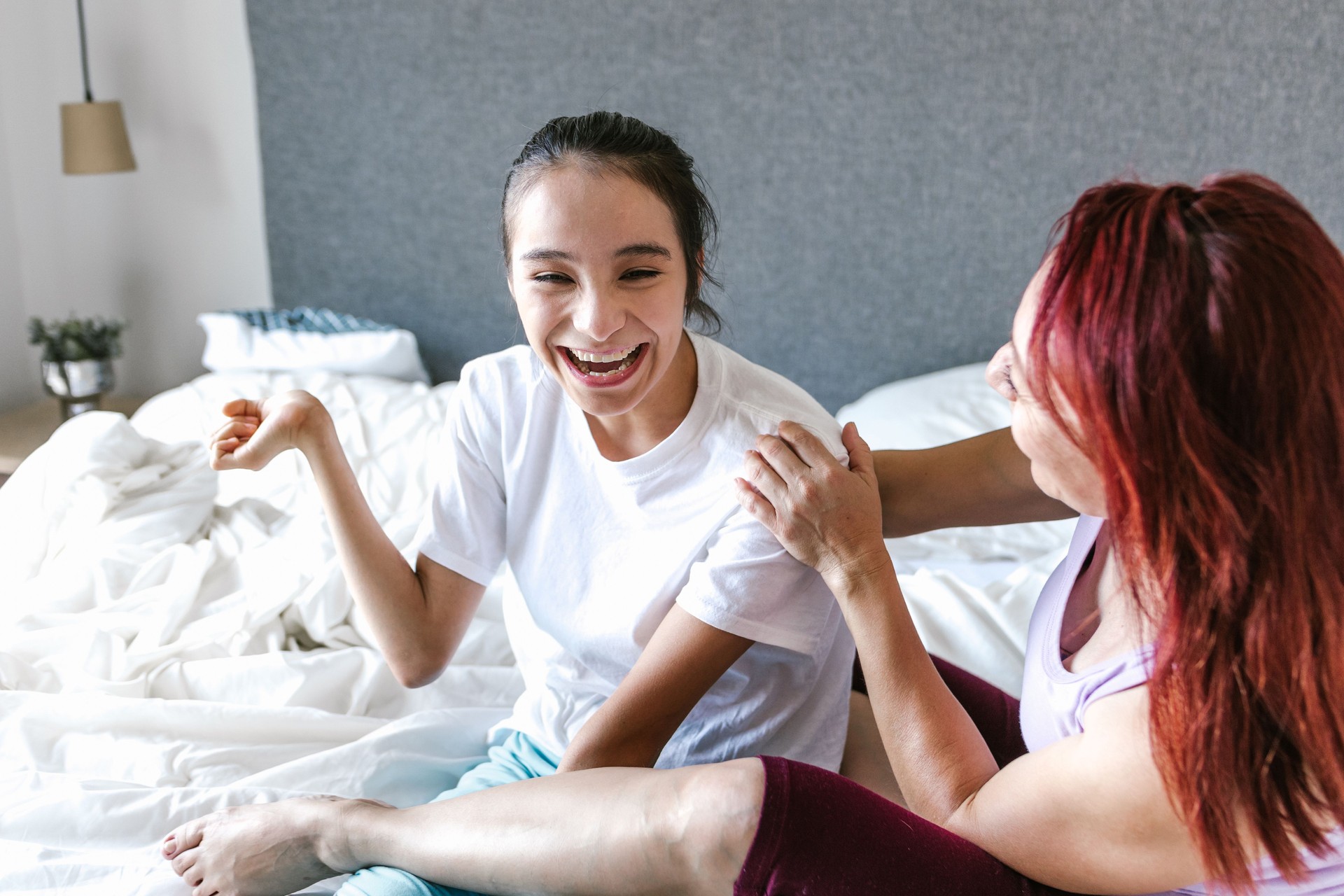Latin mother and teenage daughter with cerebral palsy laughing together on the bed at home—representing joyful caregiving, disability inclusion, and family support for teens with disabilities in Latin America